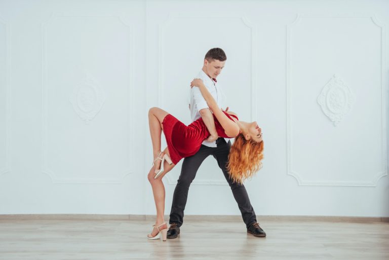 Young beautiful woman in a red dress and a man dancing, isolated on a white background.